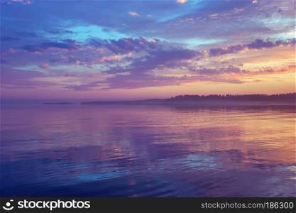 Amazing night seascape - calm water surface reflects colorful dramatic sky with purple clouds and mist floating on the horizon at sunset. White Nights season. Republic of Karelia, Russia.. Misty Purple Seascape At Sunset In The White Nights Season