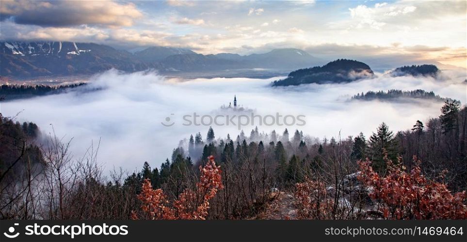 amazing panorama of Lake Bled Blejsko Jezero on a foggy morning with the Pilgrimage Church of the Assumption of Maria on a small island and Bled Castle and Julian Alps in backgroud
