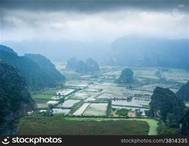 Amazing panorama view of rice fields and Vietnamese village among limestone rocks at foggy morning. Ninh Binh, Vietnam travel landscapes and destinations