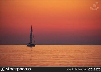 Amazing peaceful seascape of a beautiful orange sunset over Mediterranean sea, silhouette of a sail boat, sailing trip, luxury summer vacation
