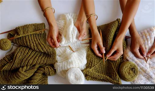Amazing scene from indoor top view, group of woman hand with knitting needles to knit wool white and mossy green scarf on white background for winter handmade gift, funny scene for winter concept