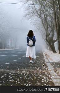 Amazing scene in early morning with girl wear backpack, standing, looking forward in fog, foggy street with petal from row of white flower along road at Da Lat city, Viet Nam