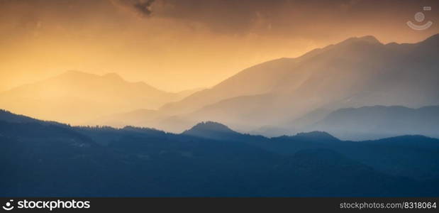 Amazing silhouettes of a mountains at colorful sunset in summer in Slovenia. Landscape with mountain ridges in fog, golden sunlight and clouds in the evening. Nature. Hills in sunlight. Scenery