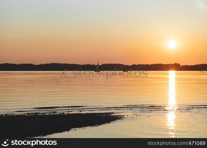 Amazing sunset in chiemsee lake with sailboat navigating