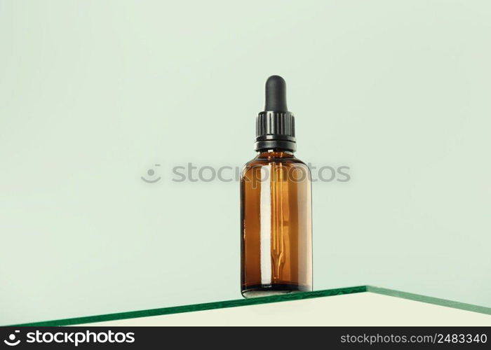 Amber glass dropper bottle with black lid on glass transparent shelf, green background. SPA natural organic beauty product packaging design, branding. Beauty salon mockup, low angle view, below the eye line, looking up, hero view