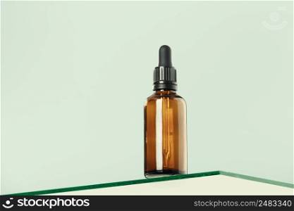 Amber glass dropper bottle with black lid on glass transparent shelf, green background. SPA natural organic beauty product packaging design, branding. Beauty salon mockup, low angle view, below the eye line, looking up, hero view
