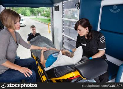 Ambulance workers caring for a senior woman with young caregiver at side