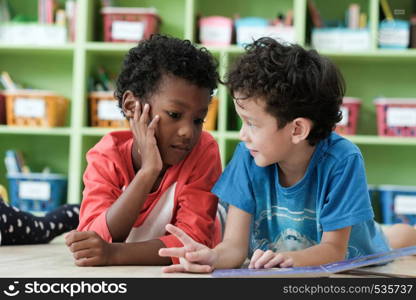 American and African boys are reading together with happiness in their kindergarten classroom, kid education and diversity concept