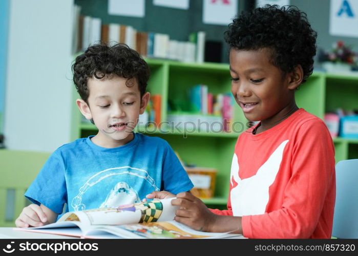 American and African boys are reading together with happiness in their kindergarten classroom, kid education and diversity concept