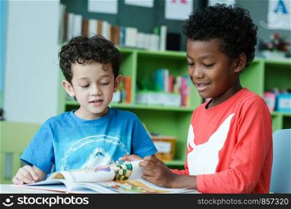 American and African boys are reading together with happiness in their kindergarten classroom, kid education and diversity concept
