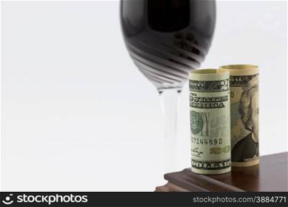 American currency placed on polished wood box in front of stem glass with red wine; horizontal image with white copy space;