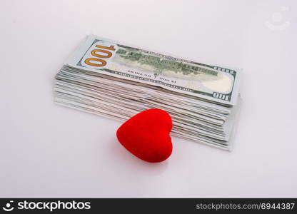 American dollar banknotes by the side of a red color heart shaped object on white background