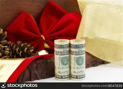 American dollars, a holiday bonus and gift, stand by rustic wooden box, red velvet ribbon, pine cones, and gold ribbon.