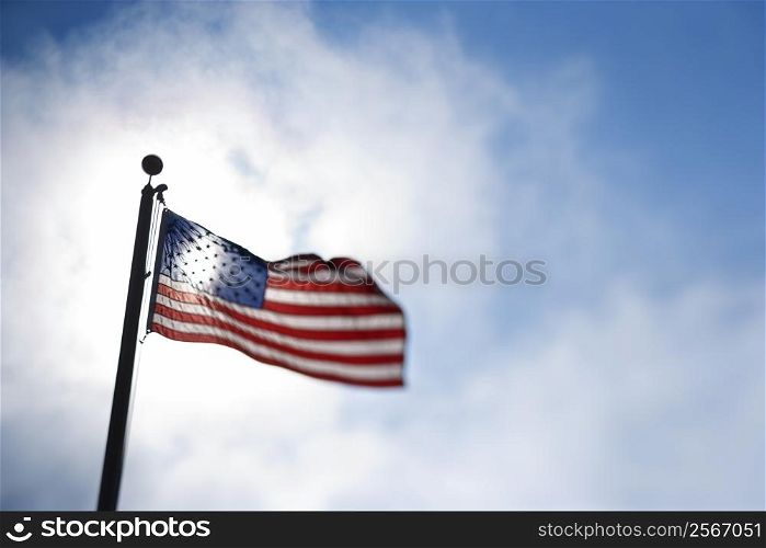American flag blowing in breeze against blue sky.