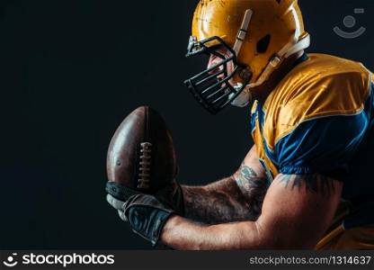 American football offensive player with ball in hand, national league, black background. Contact sport. American football offensive player with ball