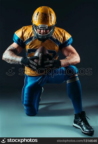 American football offensive player with ball in hand, national league, black background. Contact sport. American football offensive player with ball