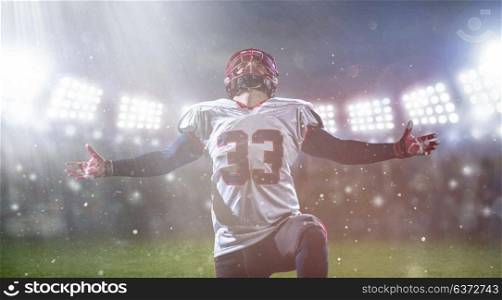 american football player celebrating after scoring a touchdown on the field of big modern stadium with lights and flares at night