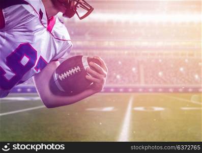 American football player holding ball while running on field of big modern stadium with flares and lights at night