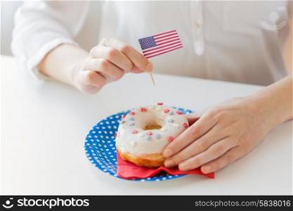 american independence day, celebration, patriotism and holidays concept - close up of female hands decorating glazed donut with american flag decoration on disposable plate at 4th july party from top