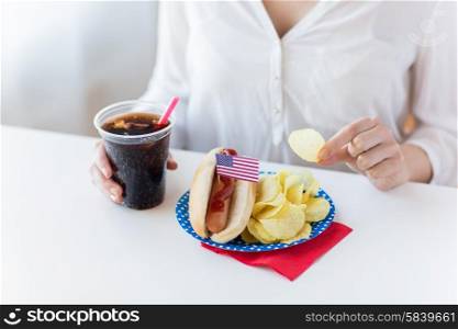american independence day, celebration, patriotism and holidays concept - close up of woman eating potato chips with hot dog and coca cola in plastic cup on 4th july at home party