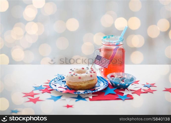american independence day, celebration, patriotism and holidays concept - close up of glazed sweet donut with flag and candies in disposable tableware at 4th july party over lights background
