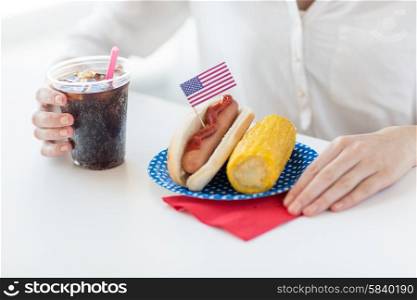 american independence day, celebration, patriotism and holidays concept - close up of woman hands with hot dog and corn holding coca cola drink in plastic cup on 4th july party