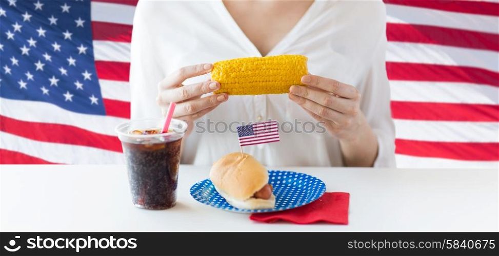american independence day, celebration, patriotism and holidays concept - close up of woman hands holding corn with hot dog and coca cola drink in plastic cup on 4th july party