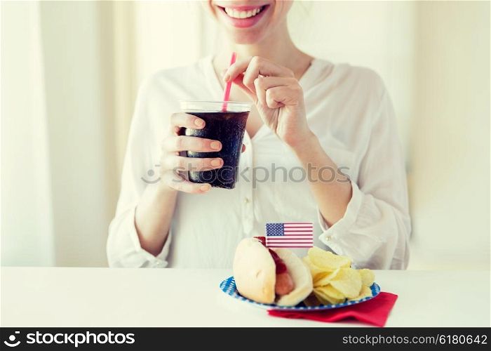 american independence day, celebration, patriotism and holidays concept - close up of happy woman drinking cola from plastic cup with hot dog and potato chips on 4th july at home party