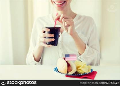 american independence day, celebration, patriotism and holidays concept - close up of happy woman drinking cola from plastic cup with hot dog and potato chips on 4th july at home party