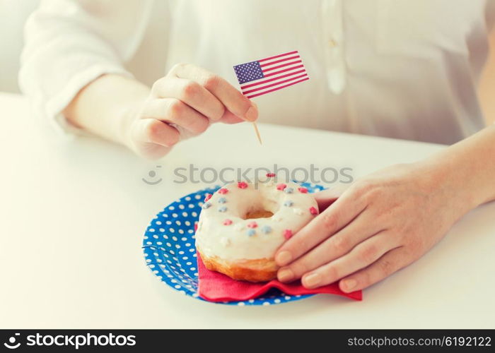 american independence day, celebration, patriotism and holidays concept - close up of female hands decorating glazed donut with american flag decoration on disposable plate at 4th july party from top