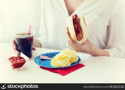 american independence day, celebration, patriotism and holidays concept - close up of woman hands holding hot dog and cola in plastic cup with potato chips and ketchup on 4th july at home party