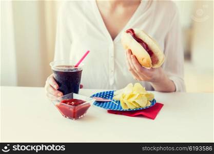 american independence day, celebration, patriotism and holidays concept - close up of woman hands holding hot dog and cola in plastic cup with potato chips and ketchup on 4th july at home party