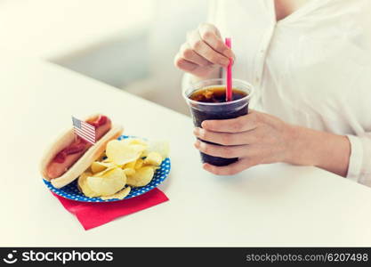 american independence day, celebration, patriotism and holidays concept - close up of woman drinking cola from plastic cup with hot dog and potato chips on 4th july at home party