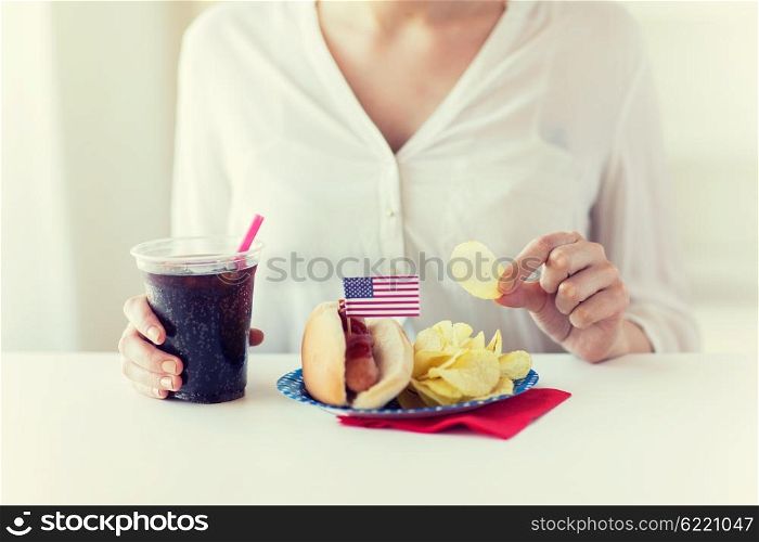 american independence day, celebration, patriotism and holidays concept - close up of woman eating potato chips with hot dog and cola in plastic cup on 4th july at home party