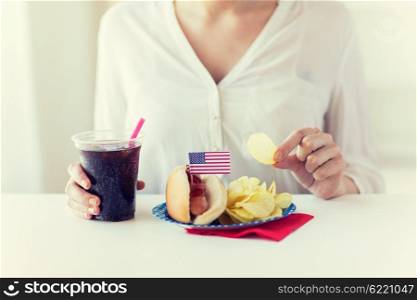 american independence day, celebration, patriotism and holidays concept - close up of woman eating potato chips with hot dog and cola in plastic cup on 4th july at home party