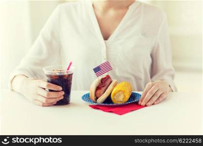 american independence day, celebration, patriotism and holidays concept - close up of woman hands with hot dog and corn holding cola drink in plastic cup on 4th july party