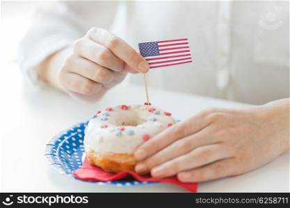 american independence day, celebration, patriotism and holidays concept - close up of female hands decorating glazed donut with american flag decoration on disposable plate at 4th july party from top