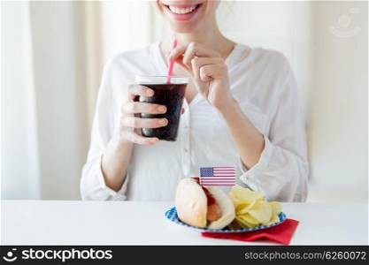 american independence day, celebration, patriotism and holidays concept - close up of happy woman drinking coca cola from plastic cup with hot dog and potato chips on 4th july at home party