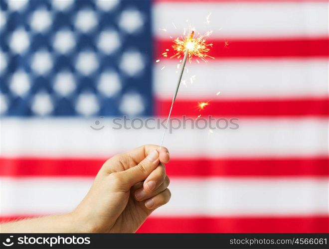 american independence day, patriotism, holidays and people concept - close up of hand holding sparkler over national flag