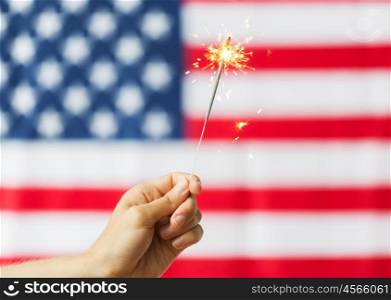american independence day, patriotism, holidays and people concept - close up of hand holding sparkler over national flag