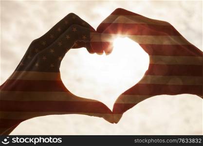 American USA flag hand heart shape silhouette made against the sun and sky of a sunrise or sunset