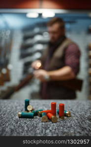 Ammo on counter, man loads a rifle on background, gun shop. Euqipment for hunters on stand in weapon store, hunting and sport shooting hobby. Ammo on counter, man loads a rifle on background