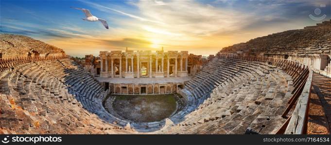 Amphitheater in ancient city of Hierapolis and seagull above it. Dramatic sunset sky. Unesco Cultural Heritage Monument. Pamukkale, Turkey. Amphitheater in ancient city of Hierapolis and seagull above it
