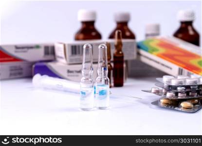 Ampoules and syringe for injection with tablets and bottles on a white table. Syringe, ampoules and medical preparations on white table