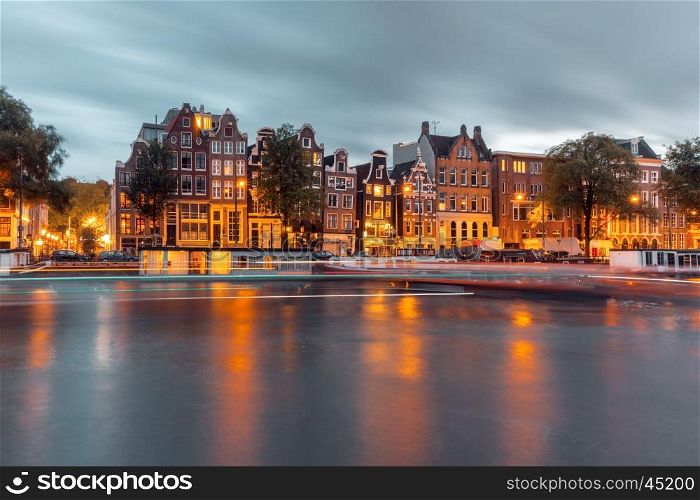 Amsterdam canal Amstel with typical dutch houses, houseboat and luminous track from the boat during twilight blue hour, Holland, Netherlands.