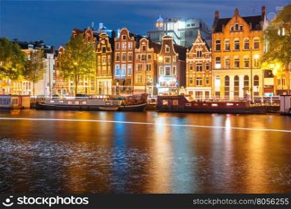 Amsterdam canal Amstel with typical dutch houses, houseboat and luminous track from the boat at night, Holland, Netherlands.