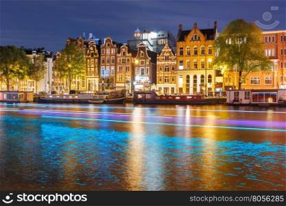 Amsterdam canal Amstel with typical dutch houses, houseboat and luminous track from the boat at night, Holland, Netherlands.