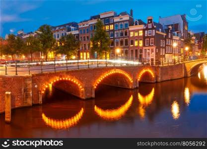 Amsterdam canal Reguliersgracht, bridge and typical houses, boats and bicycles during evening twilight blue hour, Holland, Netherlands.