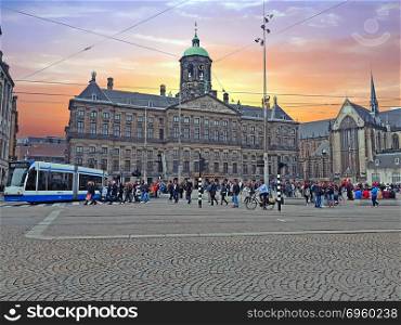 AMSTERDAM, NETHERLANDS - APRIL 9, 2018: Tourists on the Dam square in Amsterdam Netherlands at sunset. AMSTERDAM, NETHERLANDS - APRIL 9, 2018: Tourists on the Dam squa