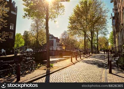 Amsterdam street with canal and old houses and bicycle on sunset. Amsterda, Netherlands. Amsterdam street with canal